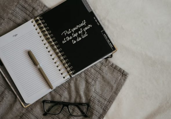 Stylish flatlay featuring a planner with quote, pen, and eyeglasses on a neutral background.